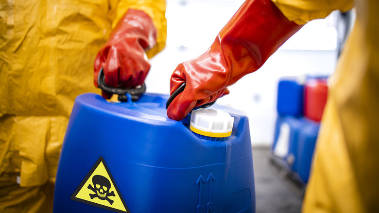 Close up view of plastic canister with toxic material carried by workers in protection suit.