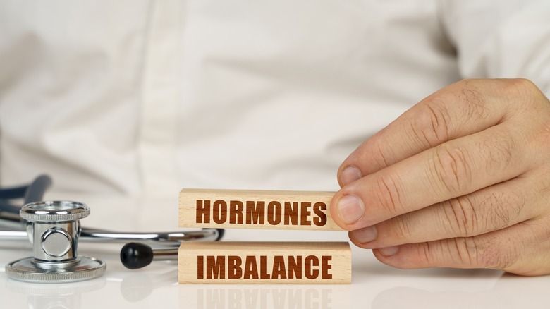 Doctor with stethoscope holding wooden chips reading "Hormones Imbalance"