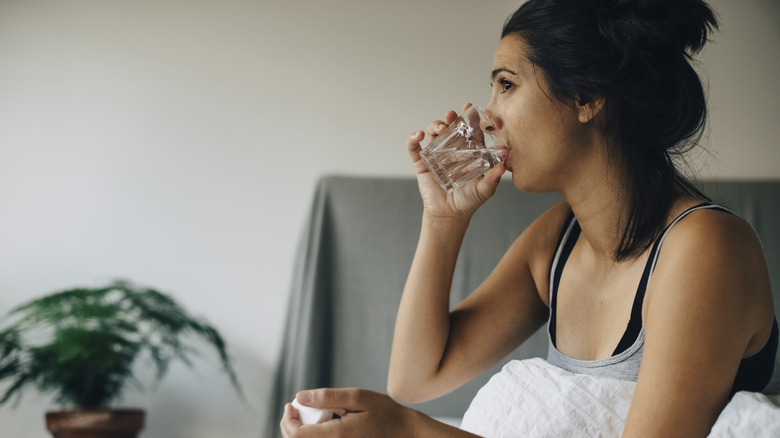 A woman drinking a glass of water in bed