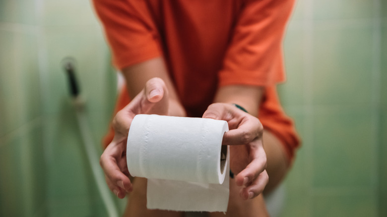 A woman sitting on the toilet holding toilet paper roll