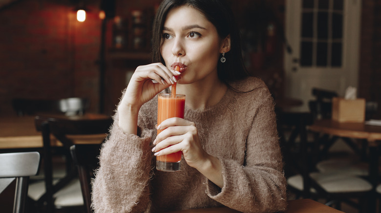 A woman sitting at a restaurant drinking carrot juice