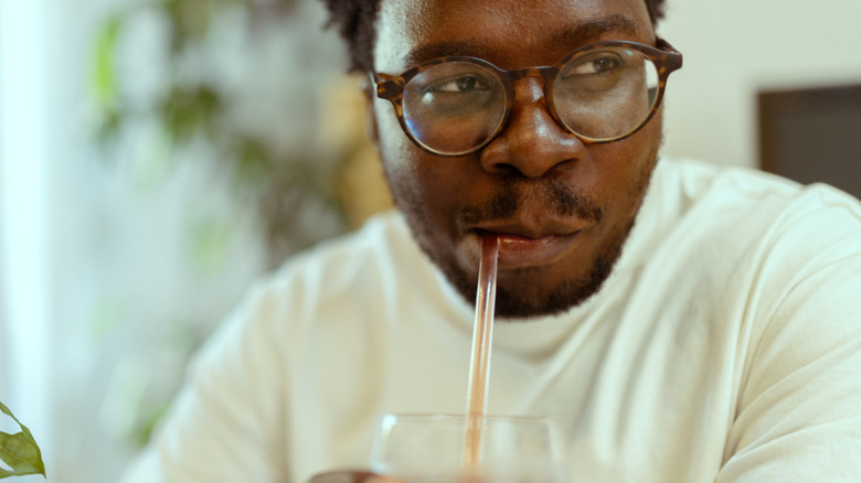 A man drinking a glass of juice with a straw