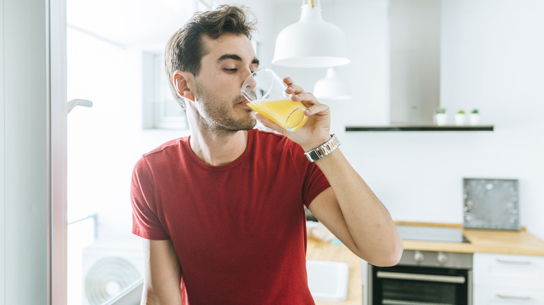 A man in his kitchen drinking orange juice