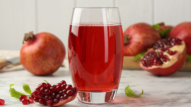 A glass of pomegranate juice sitting on a table surrounded by pomegranates