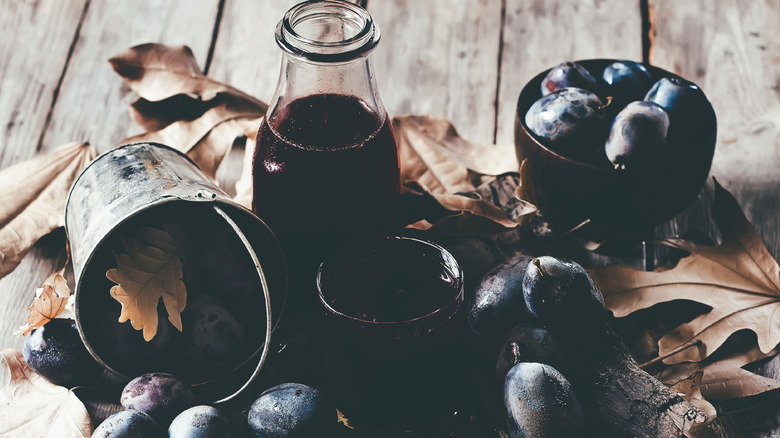 A bottle of prune juice surrounded by prunes on a porch