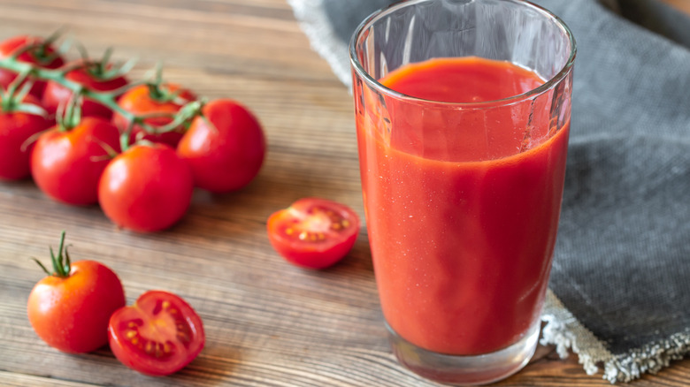 A glass of tomato juice sitting on a table with cherry tomatoes