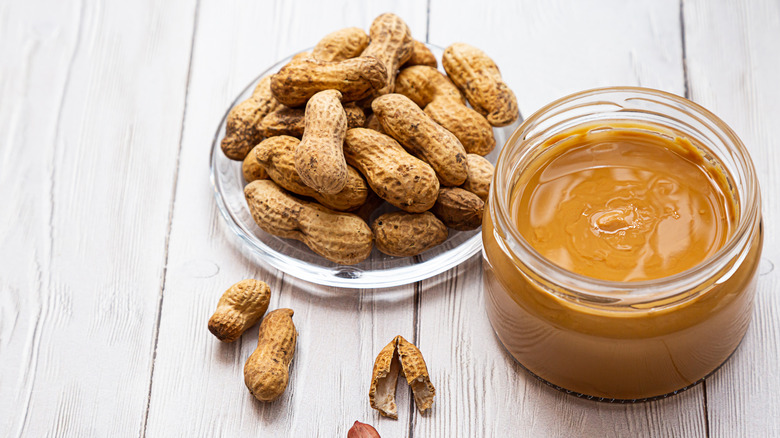 A jar of peanut butter next to a pile of peanuts