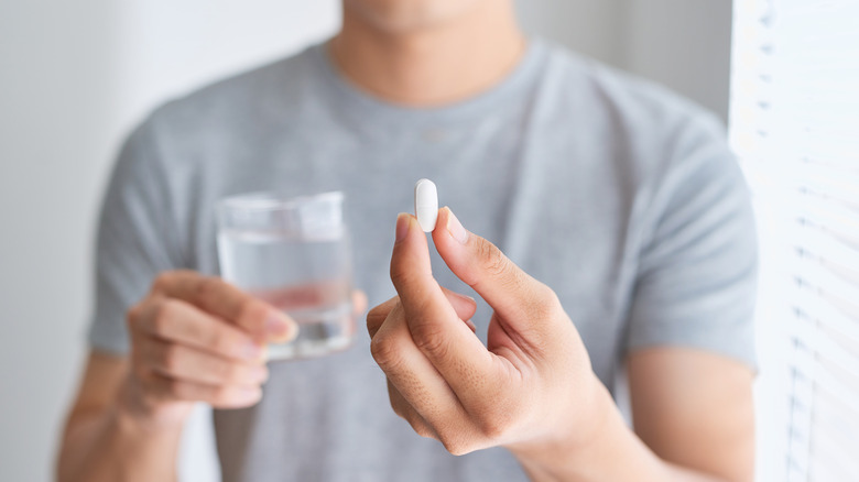 man holding pill and glass of water 