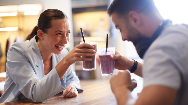 A man and a woman toast their purple smoothies in a cafe