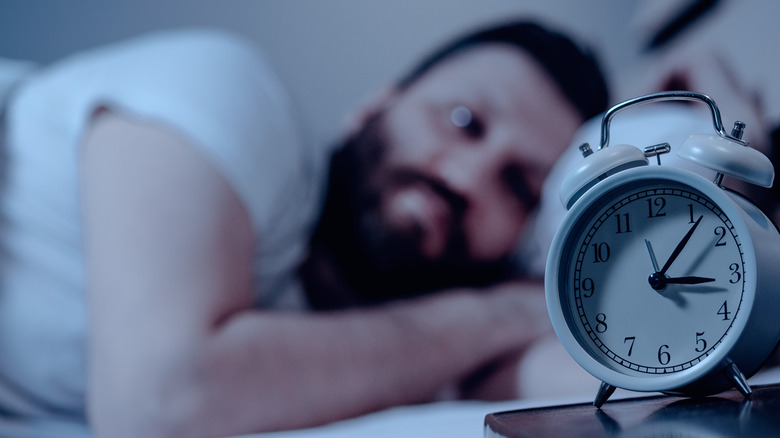 Man awake in bed staring at alarm clock