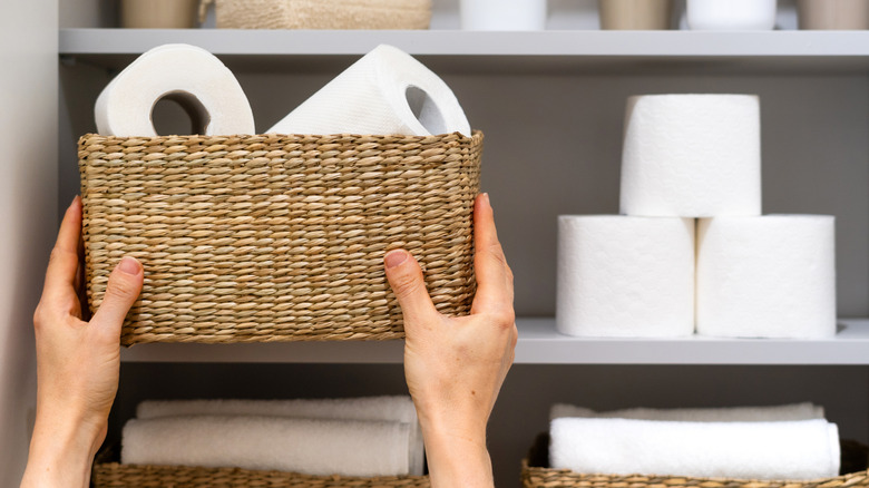 woman's hands holding basket of toilet paper rolls