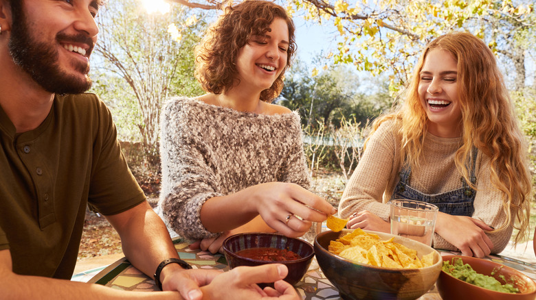 young adults eating chips and green dip outside