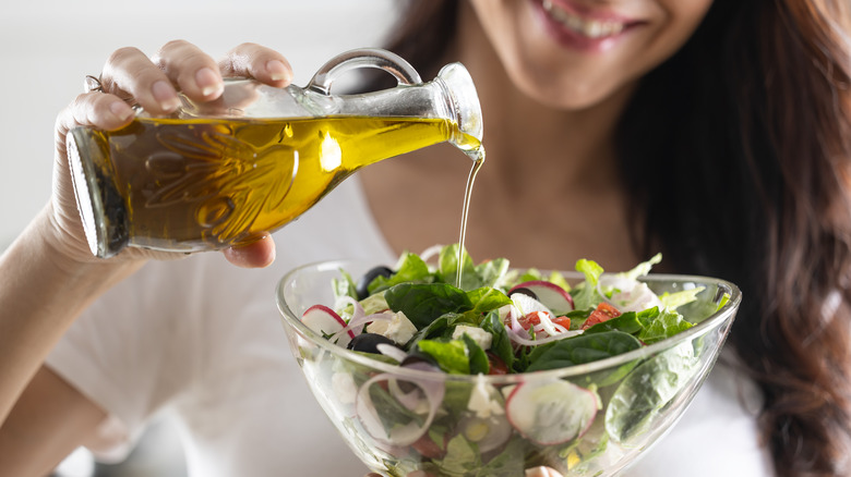 woman pouring olive oil over a salad