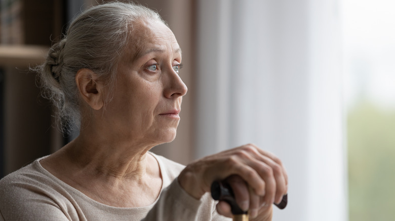 older woman looking out the window while holding a cane