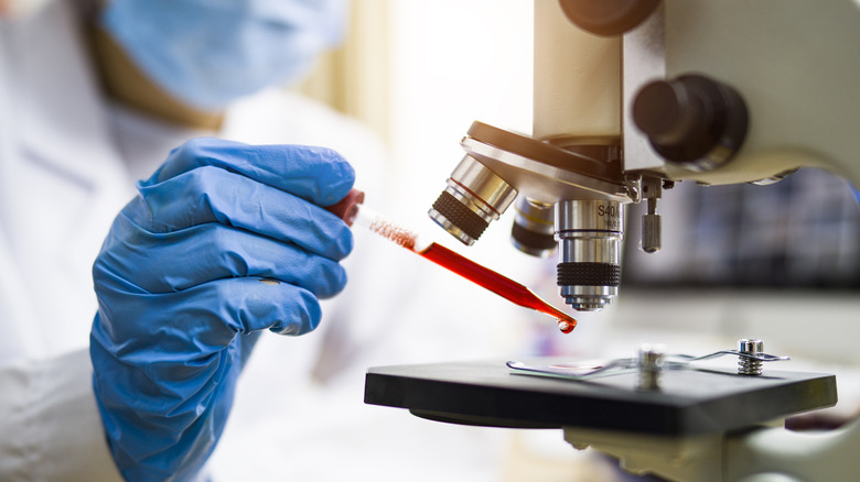 A scientist using an eyedropper to drop blood under a microscope