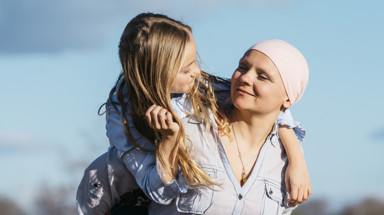 A woman with cancer wearing a scarf holds her daughter