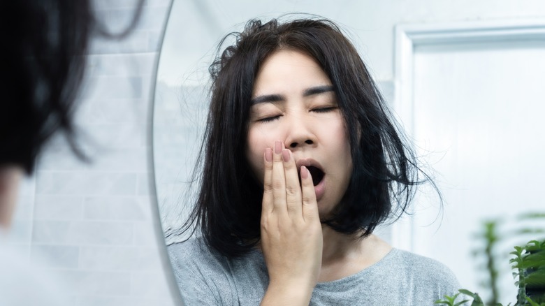 woman yawning while facing a mirror