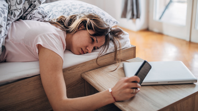 groggy woman in bed waking up to her phone's alarm 