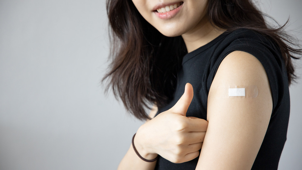 Woman with vaccination bandage on shoulder giving thumbs up