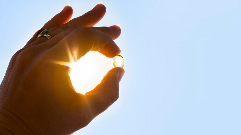 A hand holding a vitamin D supplement up to the sun