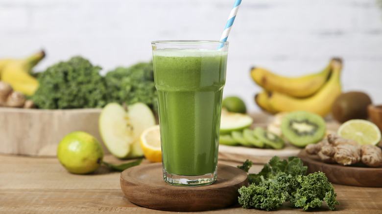 A green smoothie surrounded by kale, apples, lemon, and bananas