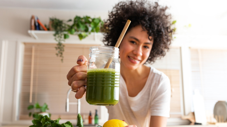 A woman holding a green smoothie with a straw