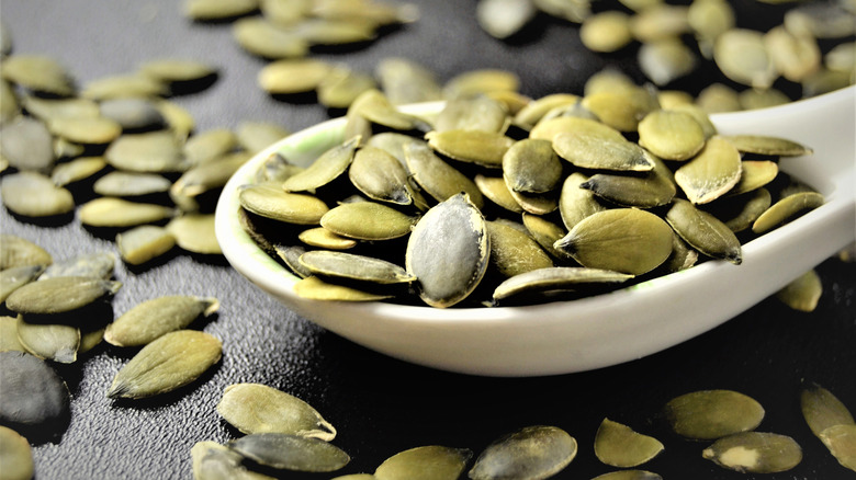 A spoonful of pumpkin seeds spilling over on a black surface