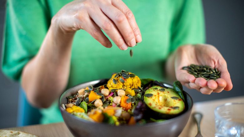 A woman's hands adding pumpkin seeds to her salad