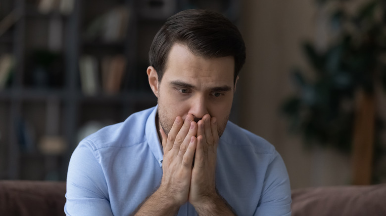 Anxious man covering mouth with hands