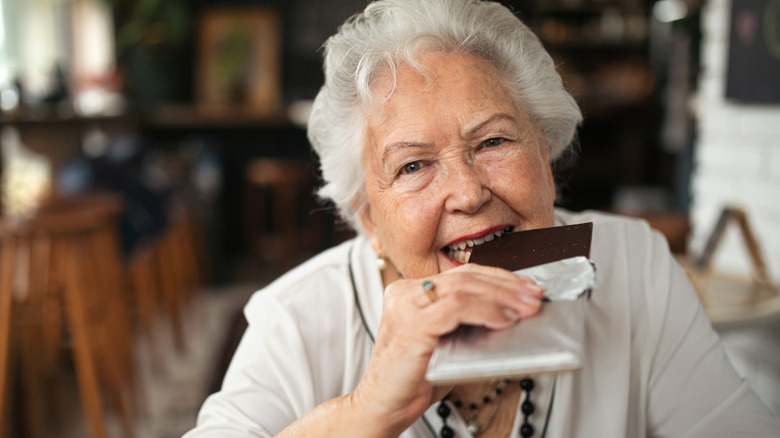 An older woman eating a large dark chocolate bar