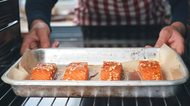 Hands placing tray of salmon filets in oven