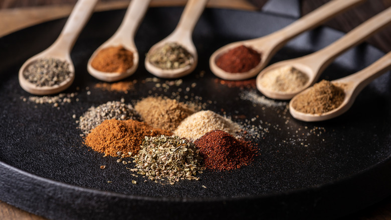 herbs and spices on wooden spoons next to piles of spices