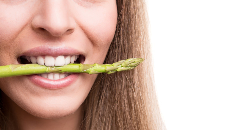 A woman biting an asparagus spear