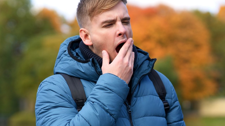 Man with jacket and backpack yawning