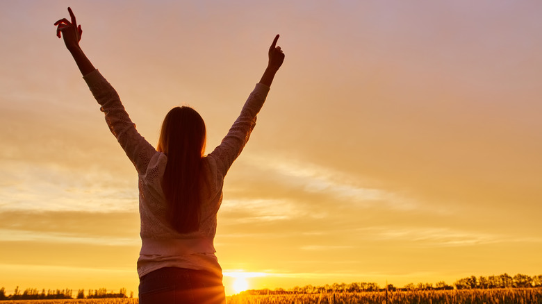 woman with arms raised at sunrise