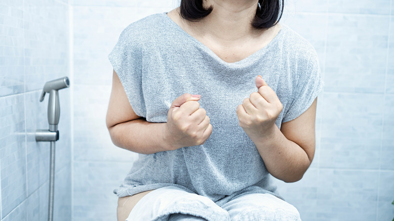 A woman sitting on the toilet in discomfort