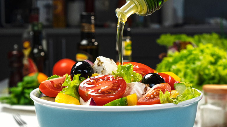 pouring olive oil over Greek salad