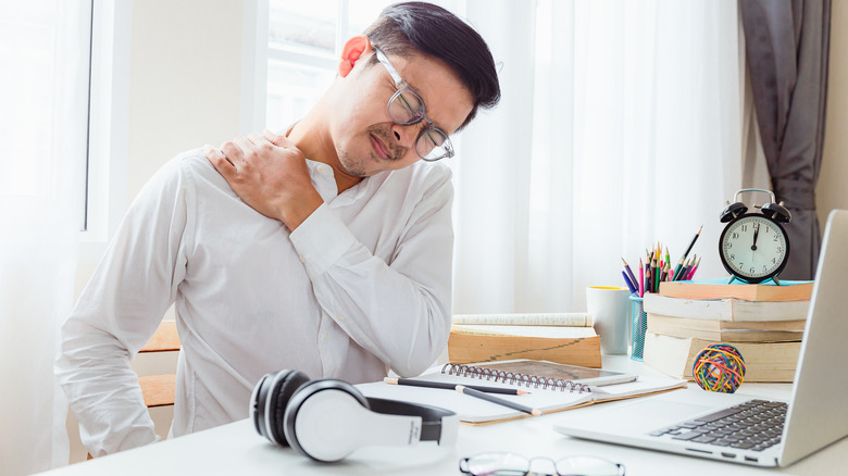 man at desk clutching his neck