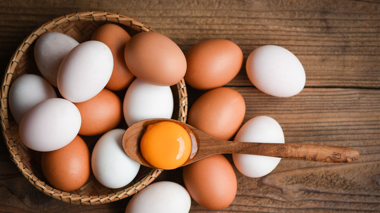 Overhead shot of chicken and duck eggs in and next to a basket, and a yolk in a wooden spoon