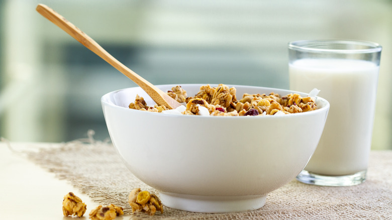 A white bowl with a wooden spoon filled with cereal next to a glass of milk