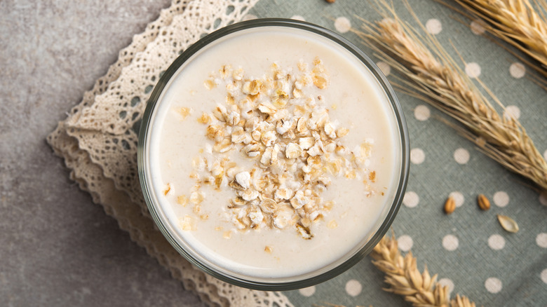 Overhead shot of oat milk with oat bits sprinkled on top and next to wheat plants