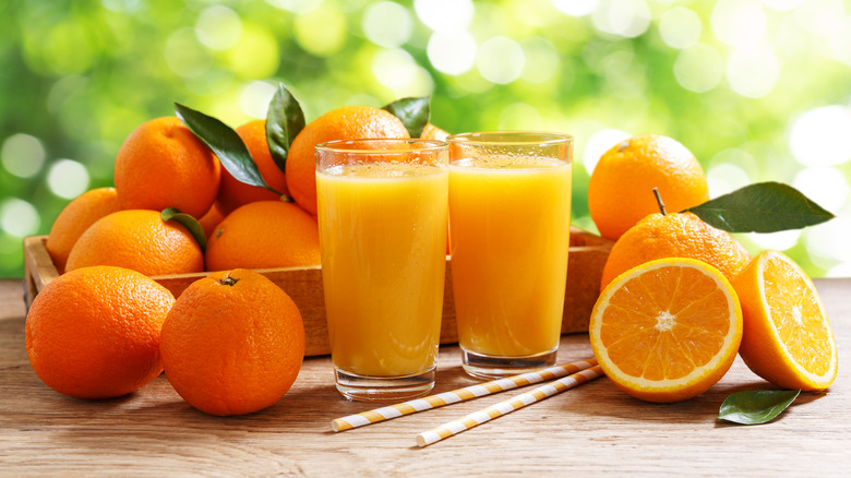 Two glasses of orange juice next to oranges and straws on a wooden surface