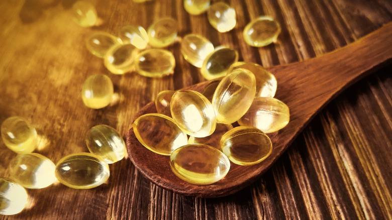 Vitamin D supplements on and next to a wooden spoon on a wooden surface