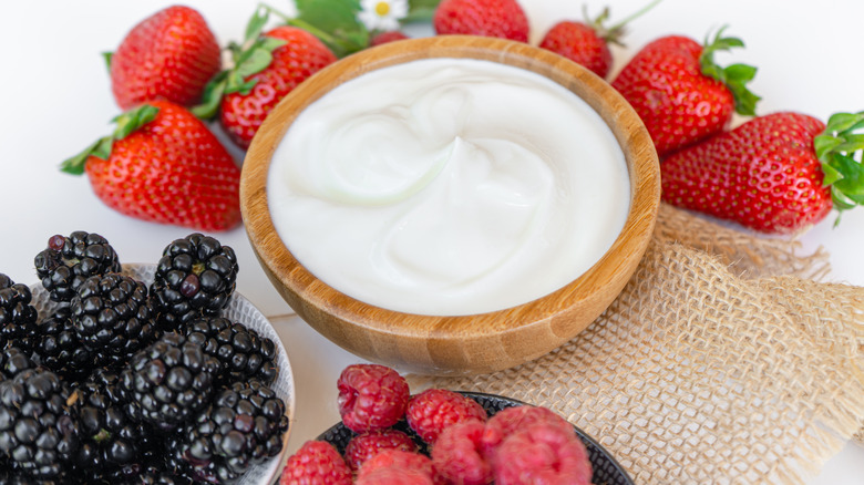 A wooden bowl filled with yogurt surrounded by strawberries, blackberries, and raspberries