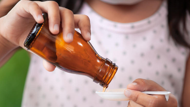 child pouring liquid medication into spoon