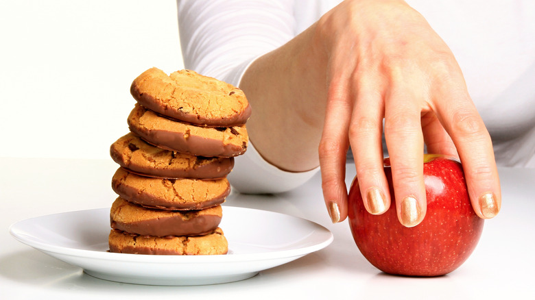 woman's hand choosing and apple over cookies