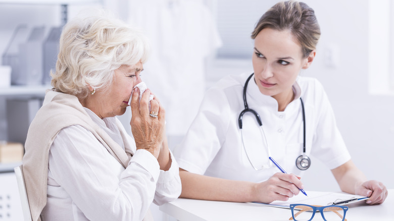 Sneezing older woman talking to doctor