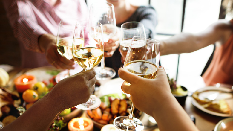 people toasting with white wine over a holiday feast