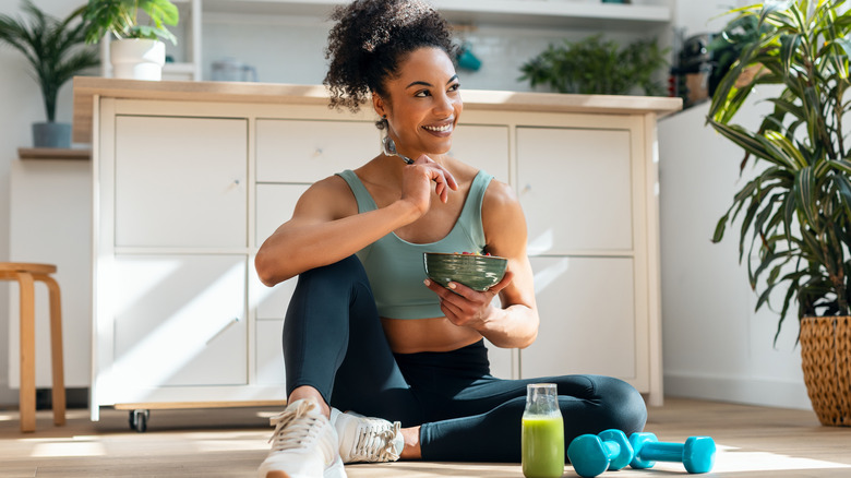 A fit woman eating from a bowl while sitting on the floor