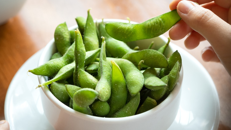 A hand reaching into a bowl of edamame